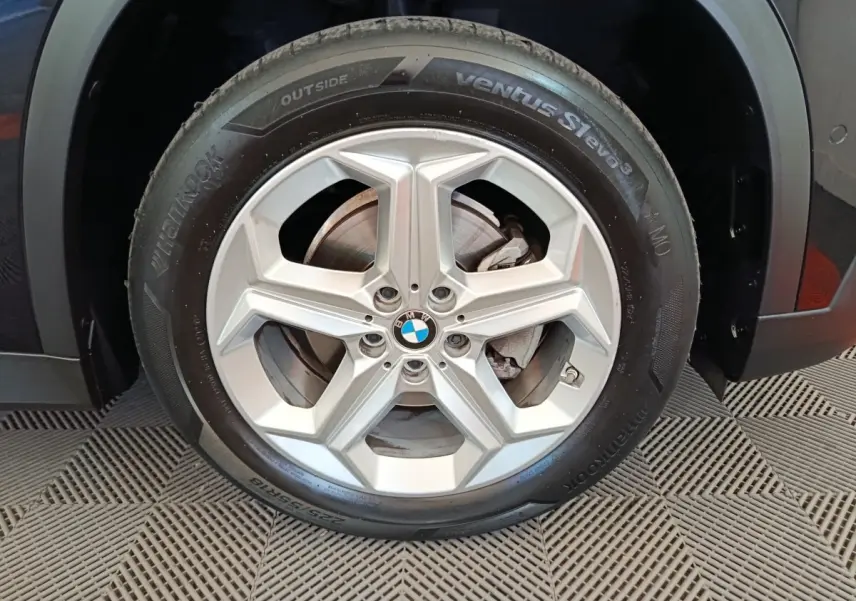 Gros plan sur la roue avant droite de la BMW X1 noire, mettant en valeur la jante alliage à cinq branches.