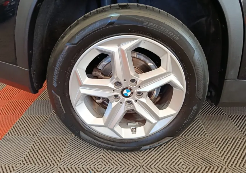 Gros plan sur la roue avant gauche noire d’un BMW X1 2023 avec jante alu cinq branches argentées.