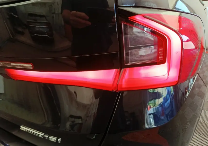 Gros plan sur le feu arrière droit rouge vif d’un BMW X1 noir sDrive18i, avec reflet de l’environnement sur la carrosserie.