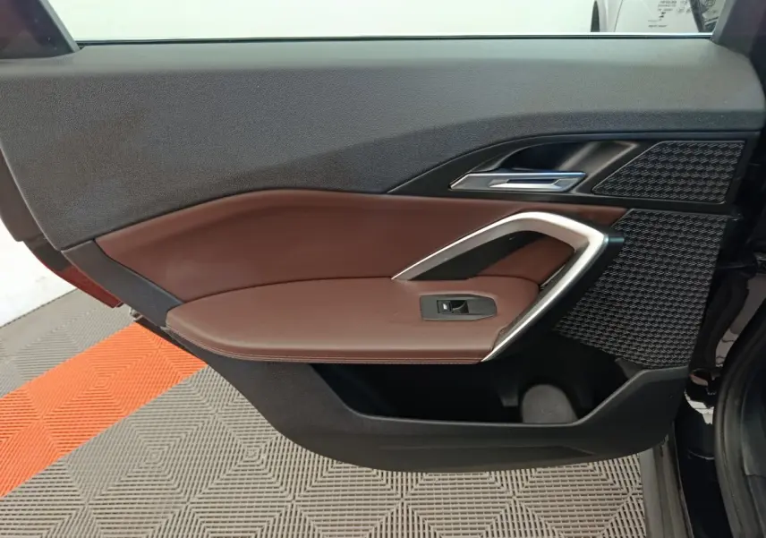 Gros plan sur la porte avant gauche intérieure du BMW X1 noir, avec garniture marron et insert argenté.