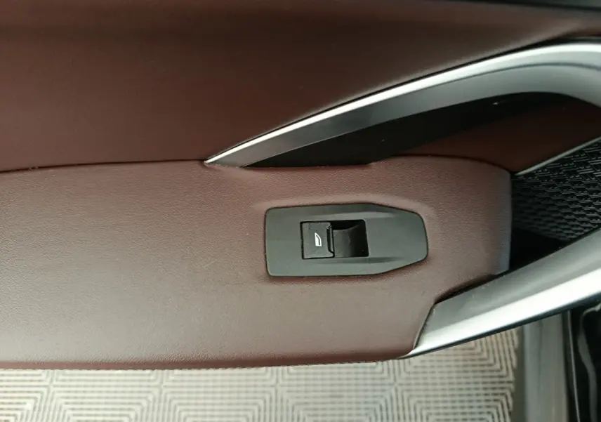 Détail de la commande de lève-vitre sur la porte côté conducteur en cuir marron du BMW X1 noir 2023.