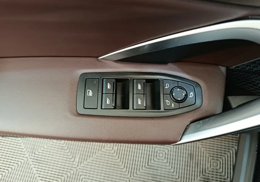 Vue rapprochée des commandes de lève-vitres et rétroviseurs sur la porte côté conducteur en cuir marron du BMW X1 noir 2023.