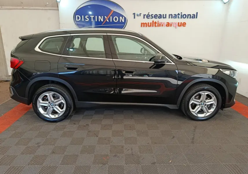 BMW X1 sDrive18i Business Design noir vue de profil côté gauche dans un showroom avec logo Distinxion en arrière-plan.