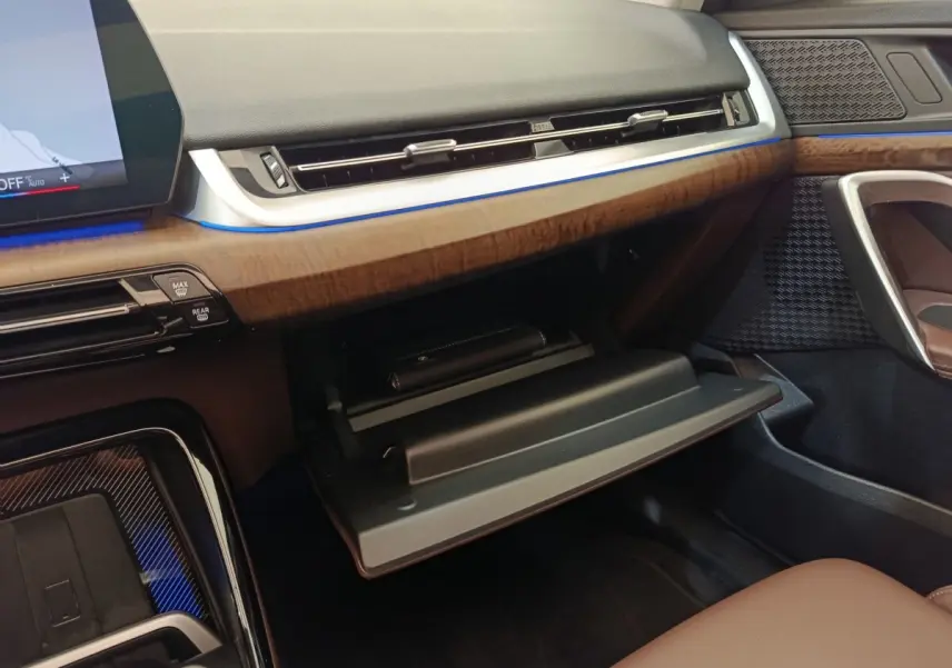 Intérieur BMW X1 2023 sDrive18i, vue côté passager sur boîte à gants ouverte et tableau de bord bois et noir.