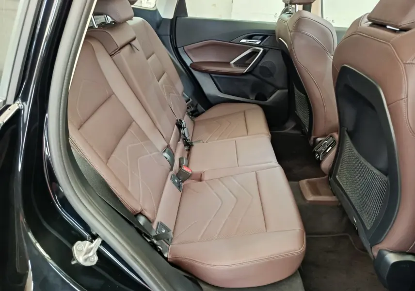 Vue intérieure côté gauche des sièges arrière en cuir marron d'une BMW X1 noire, avec banquette 3 places et rangements filet.