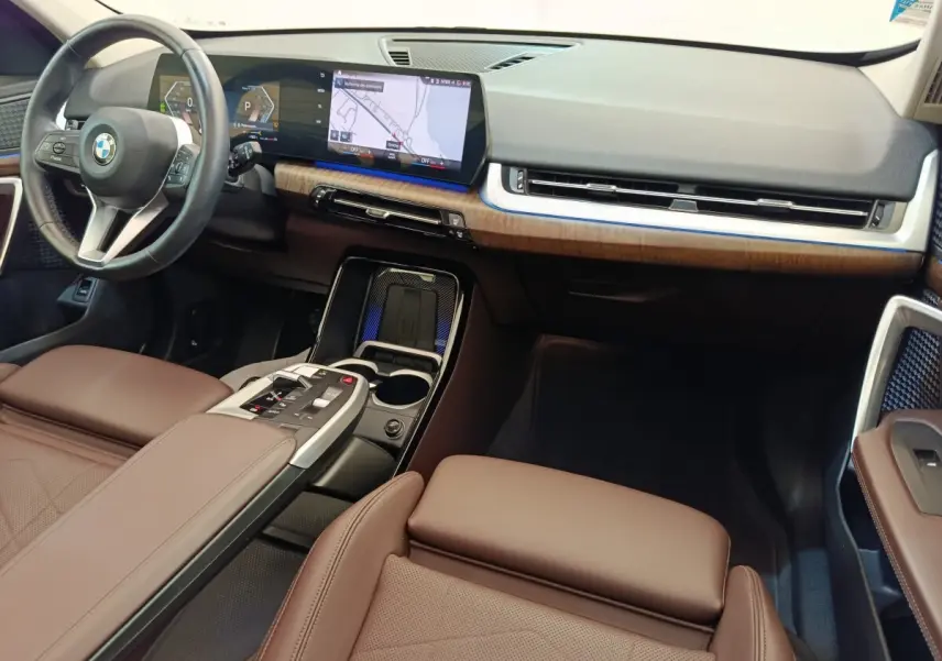 Vue intérieure avant droite du BMW X1 2023 avec tableau de bord noir, inserts bois et sièges cuir marron.