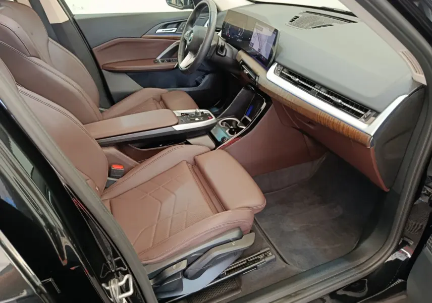 Vue intérieure côté conducteur de la BMW X1 2023 noire, sièges cuir marron et tableau de bord avec écran tactile.