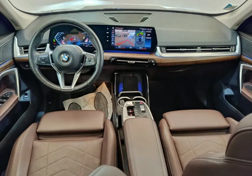 Vue intérieure avant du BMW X1 2023 avec sièges cuir marron, tableau de bord moderne et écran tactile large.