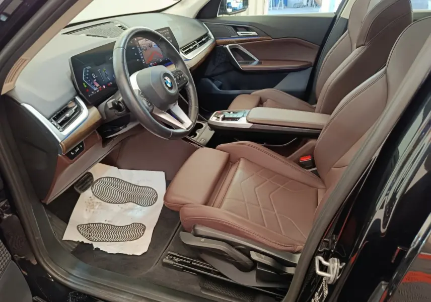 Vue intérieure côté conducteur de la BMW X1 noire 2023, sièges cuir marron et tableau de bord avec écran tactile.
