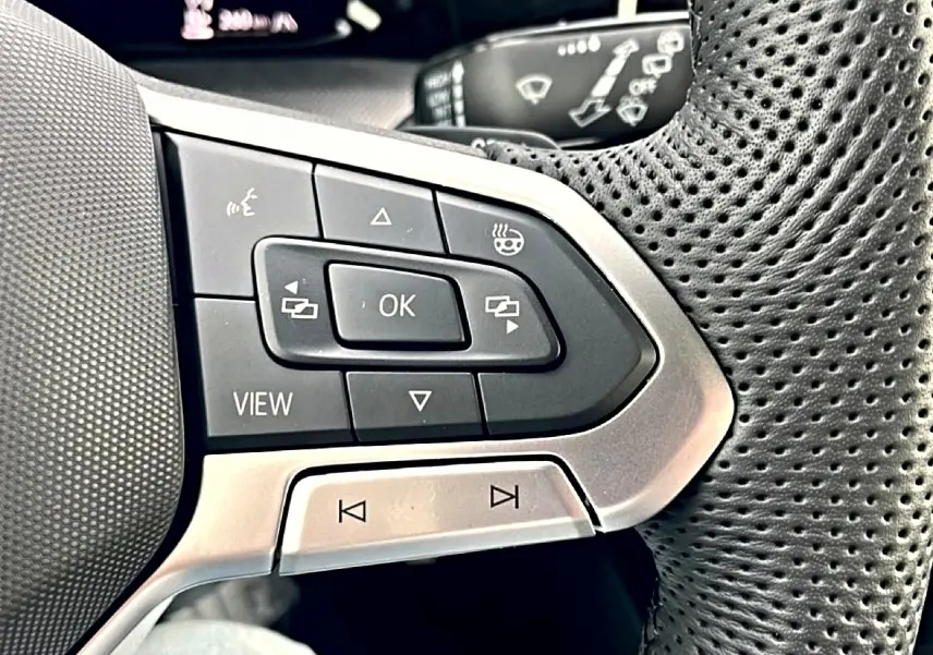 Gros plan sur les commandes multifonctions à gauche du volant perforé noir de la Volkswagen Golf 2026.