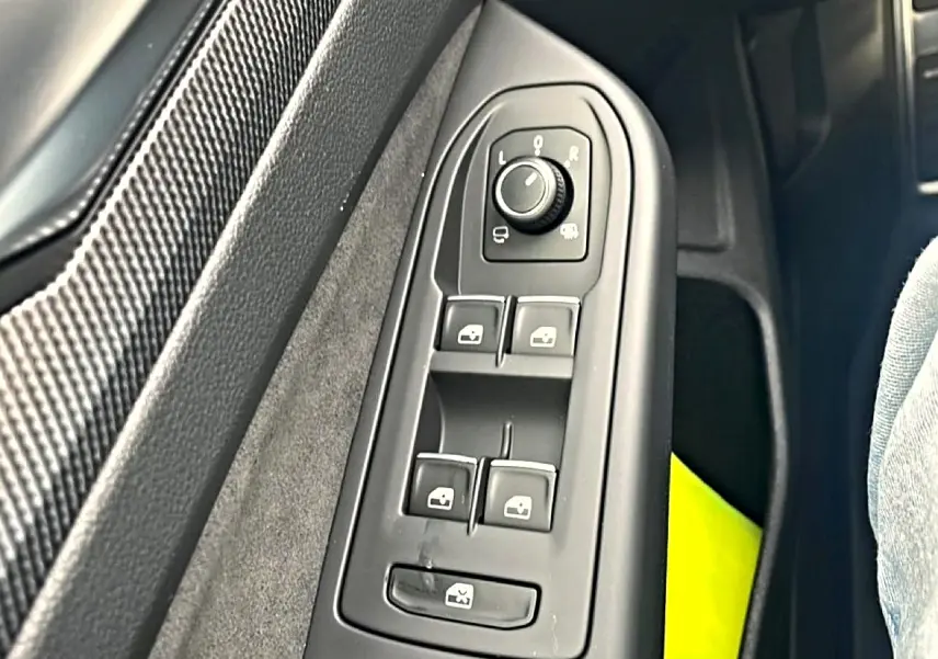 Gros plan sur les commandes de lève-vitres et rétroviseurs côté conducteur d’une Volkswagen Golf noire.