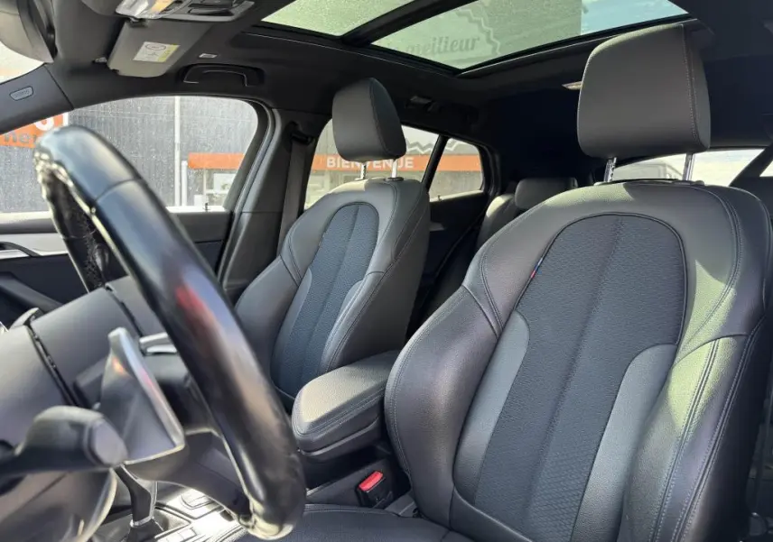 Vue intérieure du BMW X2 M Sport 2021 montrant sièges avant en cuir noir et toit ouvrant panoramique en verre.