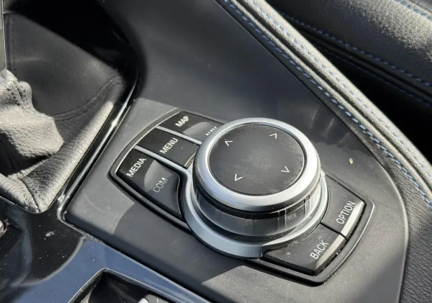 Gros plan sur la molette de commande iDrive entourée de boutons dans la console centrale en cuir noir avec surpiqûres bleues du BMW X2 jaune 2021.