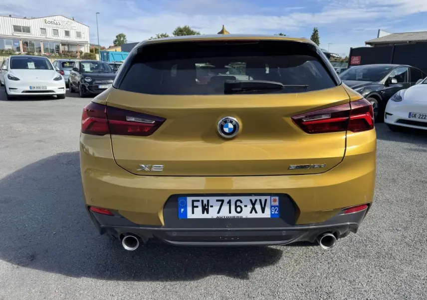 Vue arrière d'un BMW X2 sDrive 18d jaune métallisé avec double sortie d'échappement et feux arrière LED.