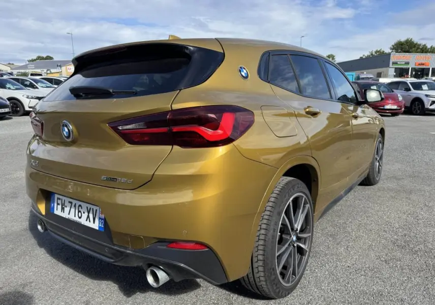 Vue 3/4 arrière droite d'un BMW X2 sDrive18d jaune métallisé avec jantes 19 pouces et double sortie d'échappement chromée.