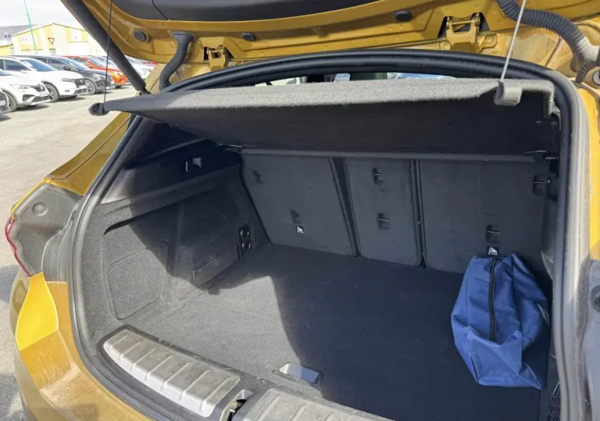 Coffre ouvert vu de l'arrière d'un BMW X2 jaune 2021 avec cache-bagages et sac bleu à droite.