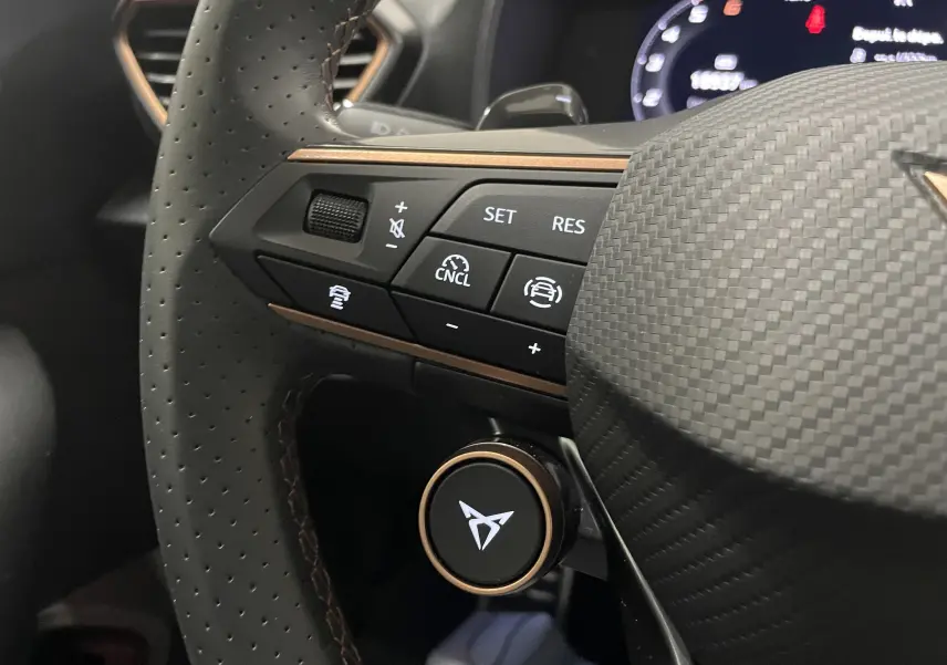 Gros plan sur le volant perforé du CUPRA Formentor 2025 avec commandes intégrées et logo lumineux au centre.