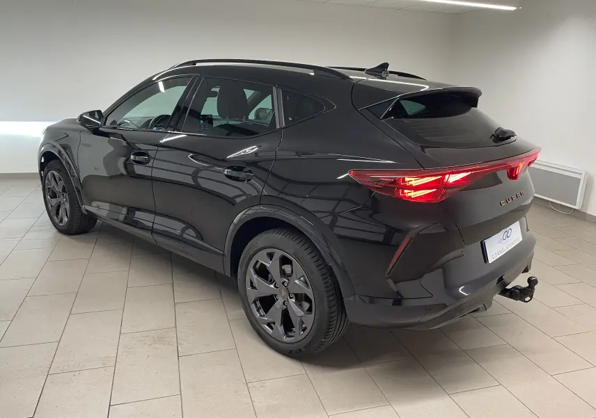 Vue 3/4 arrière droite du CUPRA Formentor noir minuit avec feux allumés et crochet d'attelage escamotable visible.