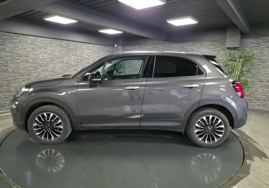 Profil droit d'un Fiat 500X gris avec jantes alliage 17 pouces et vitres surteintées dans un showroom.