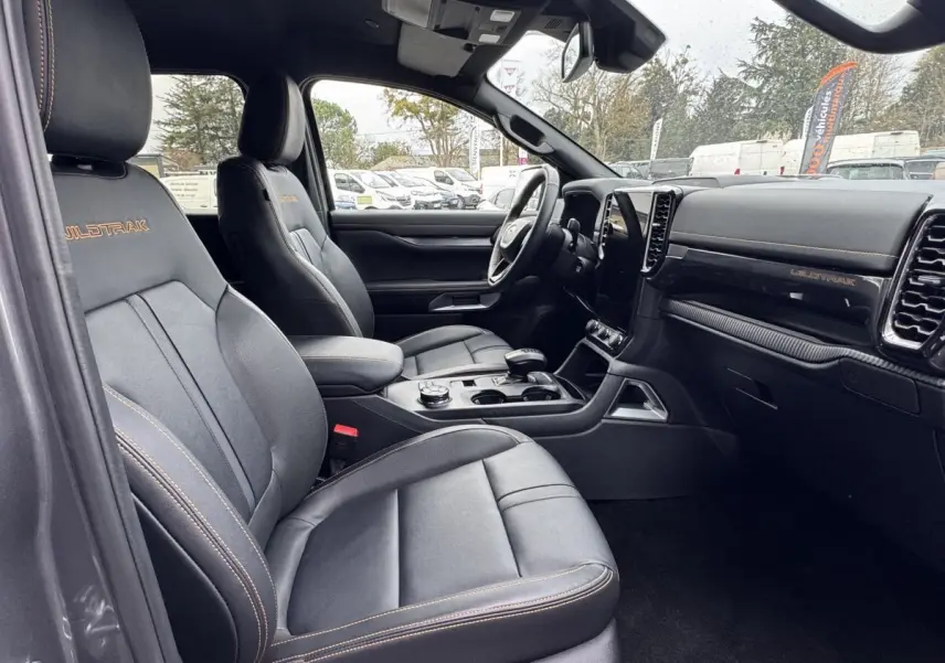 Vue intérieure côté conducteur du Ford Ranger Wildtrak 2025, sièges cuir noirs avec surpiqûres orange et tableau de bord moderne.