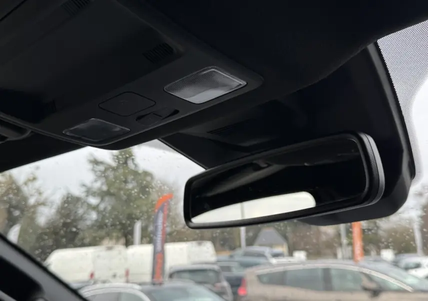 Vue intérieure centrée sur le rétroviseur intérieur et plafonnier noir du Ford Ranger 2025, arrière flou extérieur.