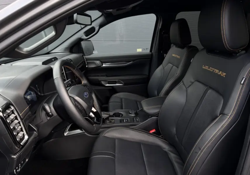 Vue intérieure côté conducteur du Ford Ranger Wildtrak 2025, sièges noirs en cuir avec surpiqûres orange et logo brodé.