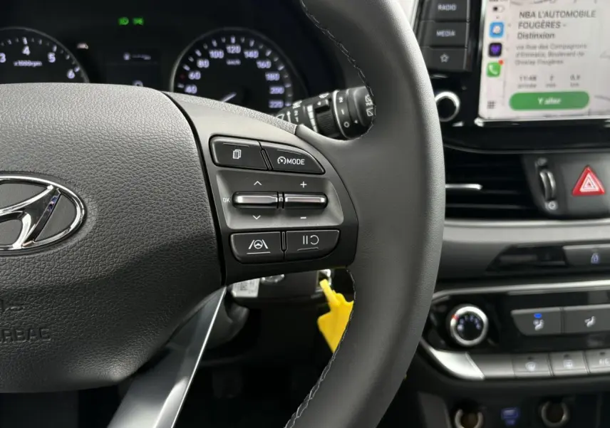 Gros plan sur le volant cuir noir de la Hyundai i30 SW T-GDI 120 Modern 2025, avec commandes intégrées et tableau de bord en arrière-plan.