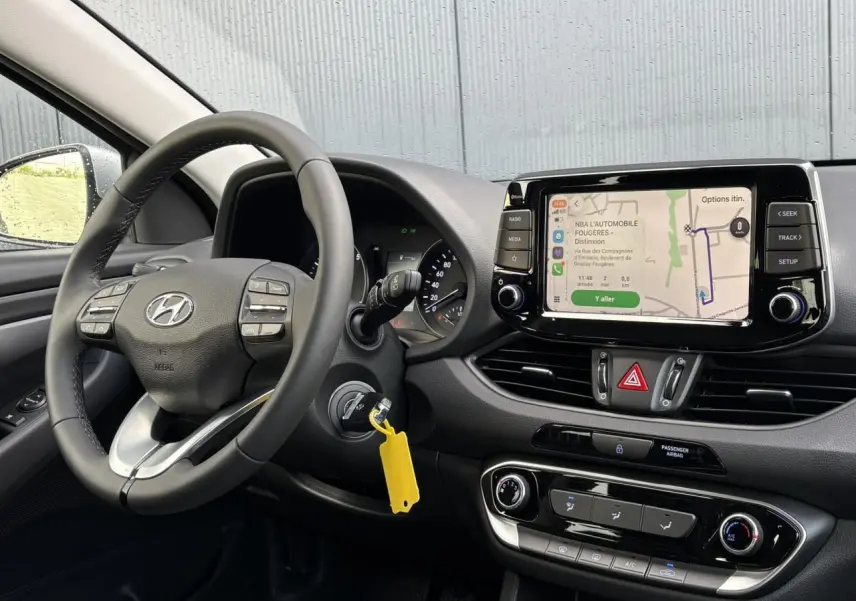Vue intérieure côté conducteur de la Hyundai i30 SW T-GDI 120 Modern 2025, tableau de bord noir avec écran tactile et volant cuir.