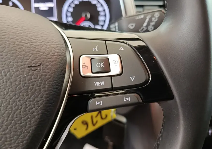Gros plan sur les commandes multifonctions à droite du volant cuir noir du Volkswagen T-Roc 1.5 TSI bleu, tableau de bord en arrière-plan.
