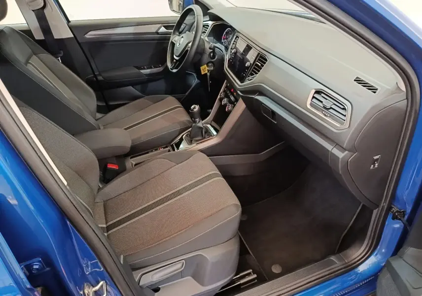Vue intérieure côté conducteur du Volkswagen T-Roc bleu 2020, montrant sièges tissu et tableau de bord moderne avec écran tactile.