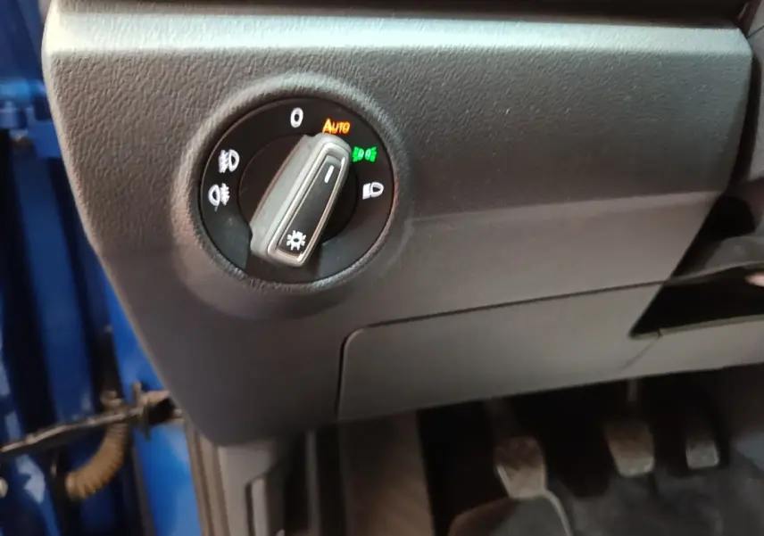 Gros plan sur le bouton de commande des phares à gauche du volant dans un Volkswagen T-Roc bleu 2020, intérieur noir.