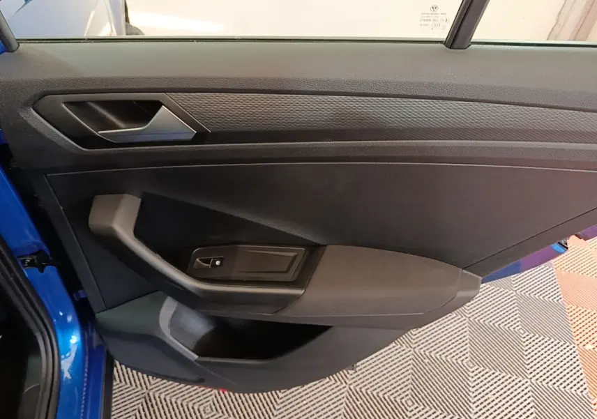Vue rapprochée de la porte avant gauche bleu vif du Volkswagen T-Roc 1.5 TSI avec poignée et commande de vitre noire.