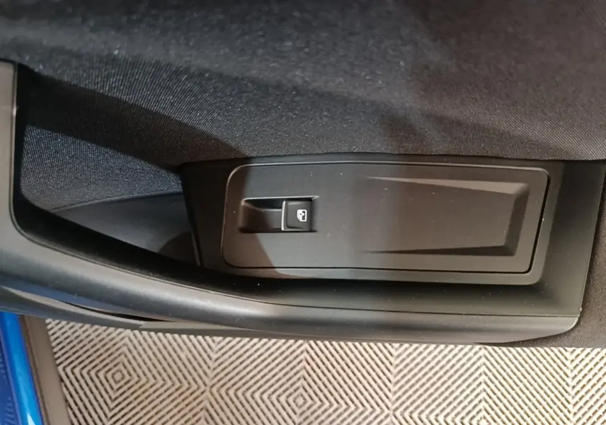 Détail de la commande d’ouverture de coffre sur la porte intérieure d’un Volkswagen T-Roc bleu.