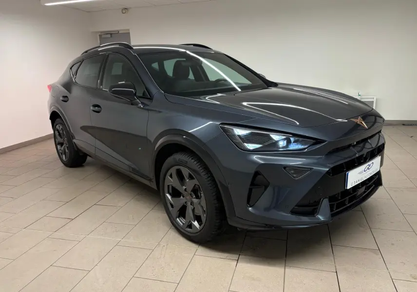 Vue 3/4 avant droit d'un CUPRA Formentor gris magnétique avec phares allumés et jantes noires en intérieur showroom.