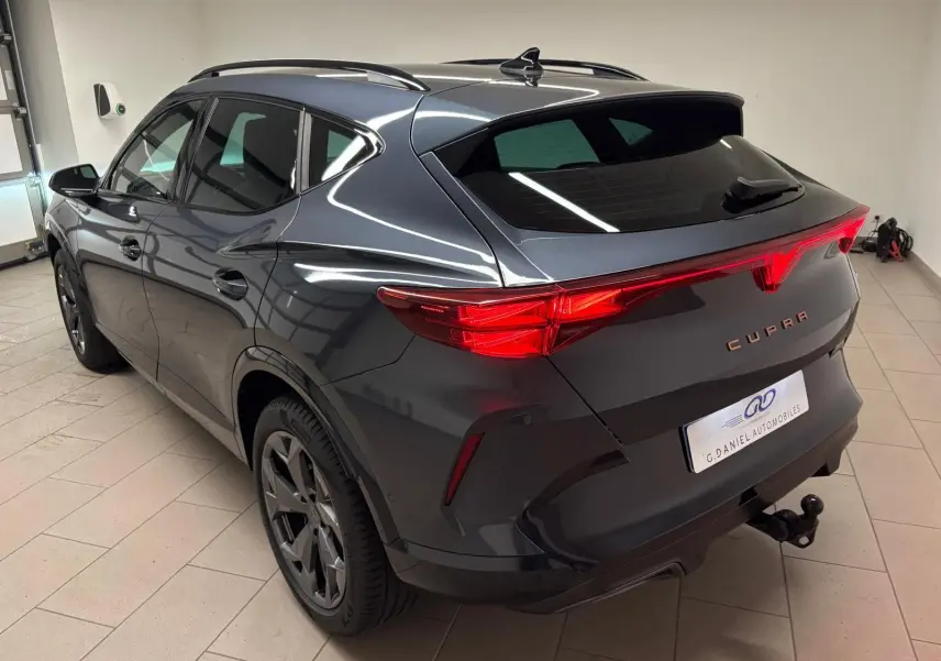 Vue 3/4 arrière droite d'un CUPRA Formentor gris magnétique avec attelage escamotable et feux arrière allumés.