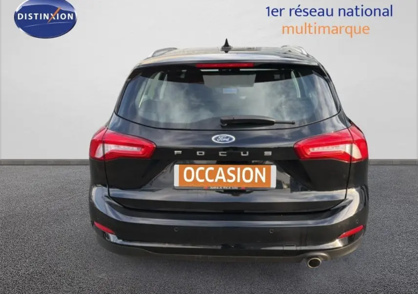 Vue arrière d'une Ford Focus SW noire de 2019 avec barres de toit et feux arrière allumés.