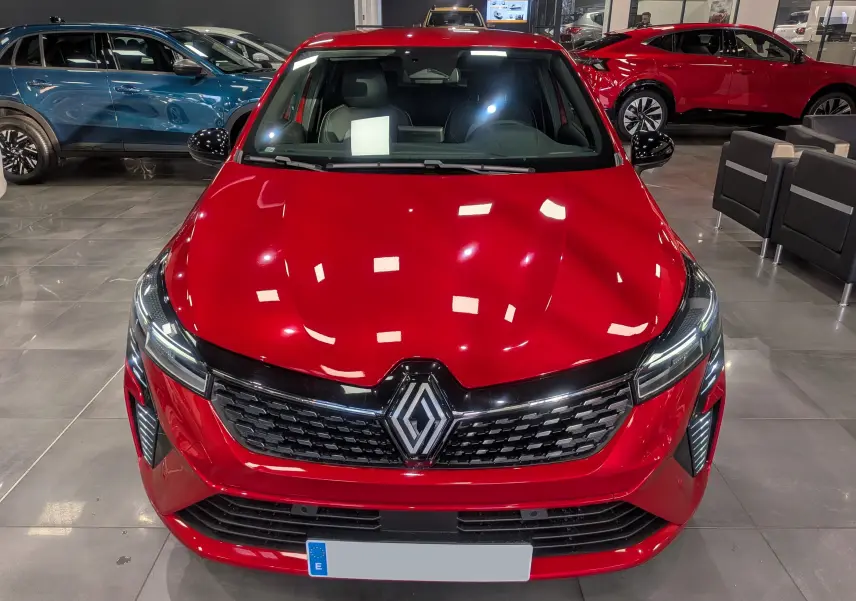 Renault Clio V Rouge Flamme vue de face en intérieur, mettant en valeur sa calandre noire et ses phares LED fins.