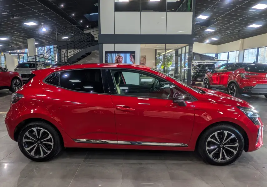 Profil côté gauche d'une Renault Clio V Rouge Flamme, avec jantes alliage et détails chromés visibles en concession.