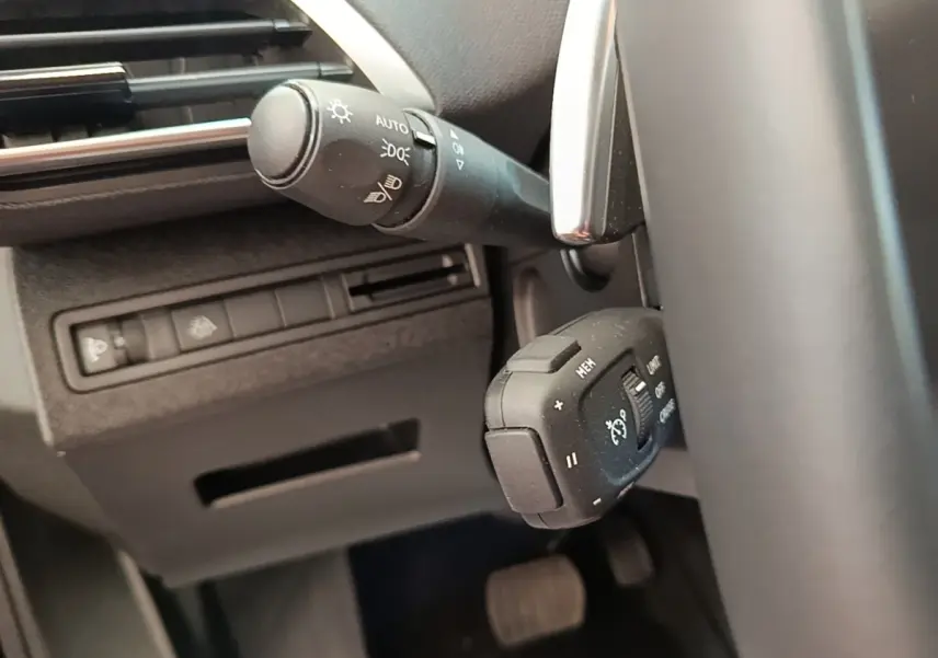 Gros plan sur les commandes du volant côté gauche du Peugeot 3008 noir, avec réglages phares et régulateur de vitesse.