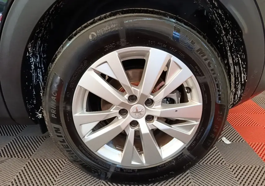 Gros plan sur la roue avant droite avec jante argentée et pneu Michelin du Peugeot 3008 noir 2022.