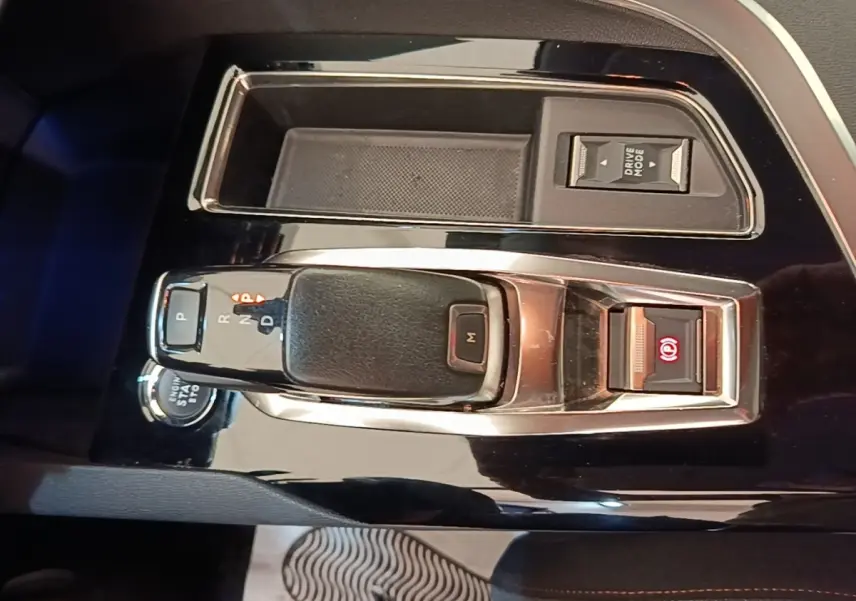 Gros plan sur la console centrale noire du Peugeot 3008 2022, avec levier de boîte auto et bouton frein électrique allumé.