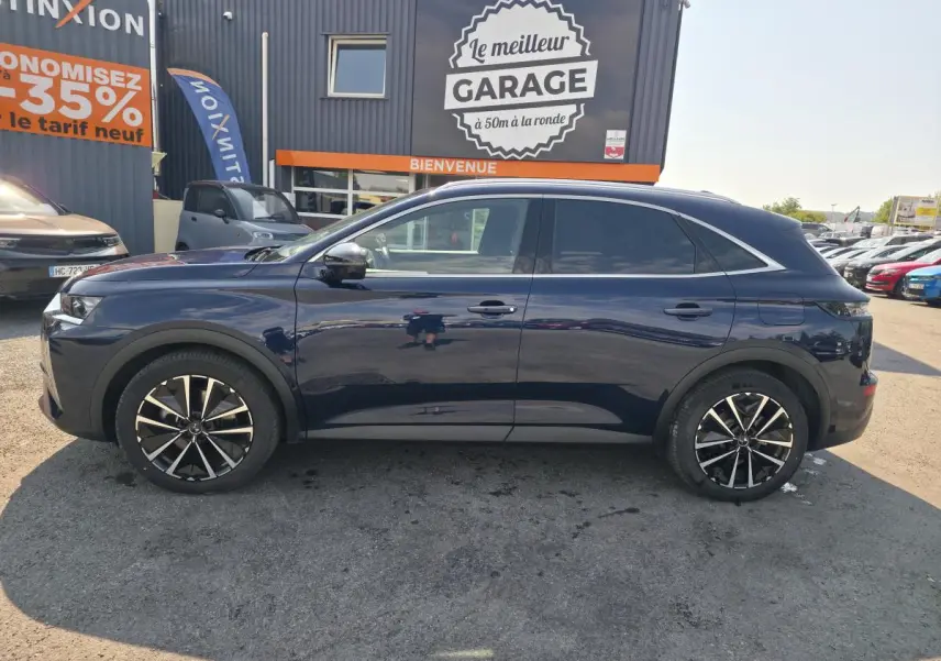 Vue latérale droite du SUV DS7 Crossback E-Tense 225 bleu métallisé avec jantes alliage 19 pouces, stationné devant un garage.