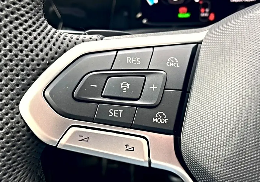 Gros plan sur les commandes de régulateur de vitesse au volant cuir perforé d'une Volkswagen Golf noire 2026.