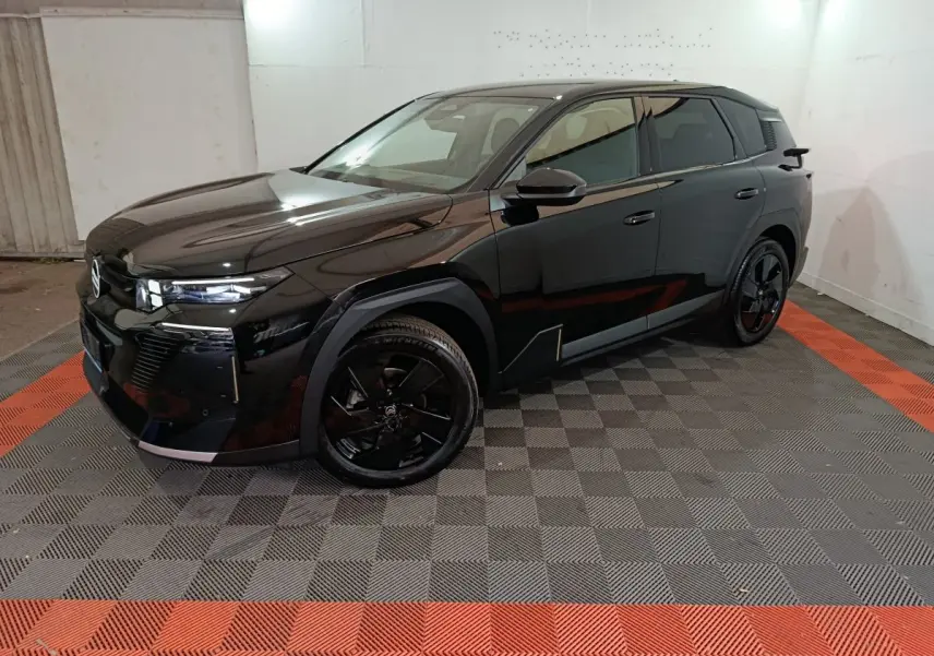 Vue 3/4 avant droite d'une Citroën C5 Hybride noire avec jantes noires et phares LED dans un garage.