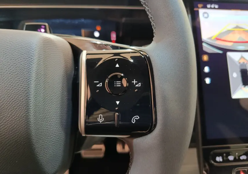 Gros plan sur la commande multifonctions noire à droite du volant cuir gris du Citroën C5 Hybride 2026, avec écran tactile en arrière-plan.