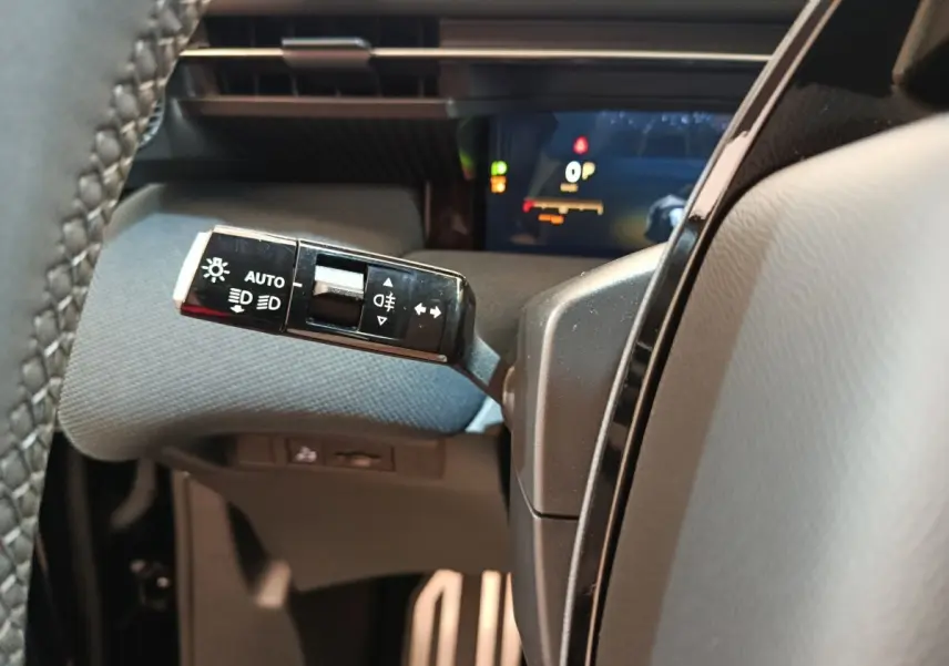Gros plan sur la commande des phares et clignotants côté gauche du volant dans l’habitacle noir du Citroën C5 Hybride 2026.