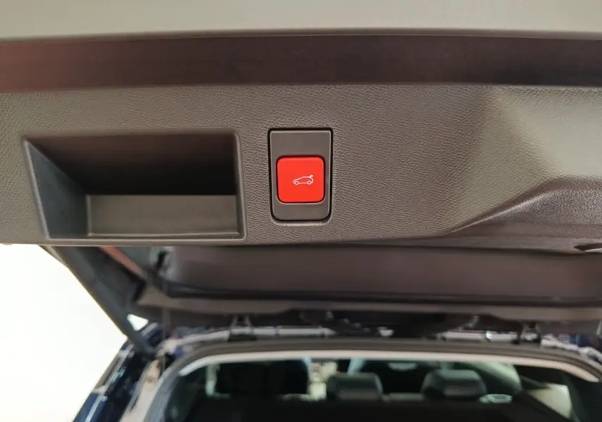 Bouton rouge d'ouverture électrique du coffre sur la partie intérieure du hayon d'une Citroën C5 noire, vue arrière ouverte.