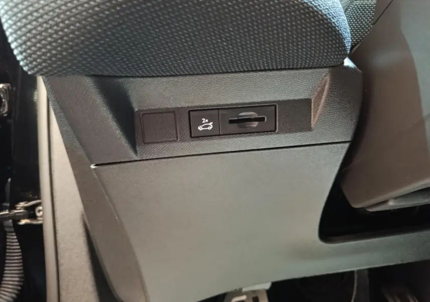 Gros plan sur le bouton d'ouverture du coffre sous le siège avant dans l'habitacle noir du Citroën C5 hybride 2026.