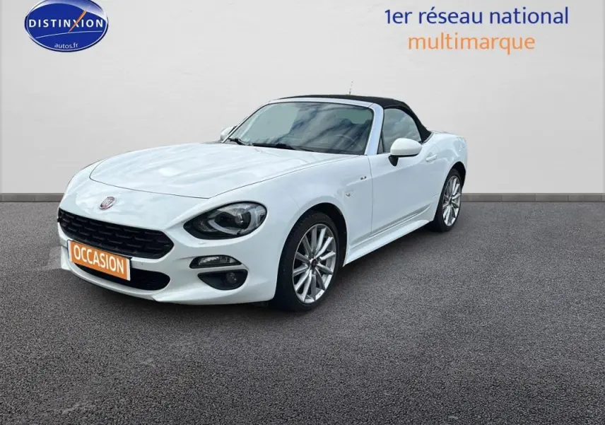 Fiat 124 Spider blanc vue 3/4 avant avec capote noire et jantes alliage 17 pouces sur sol gris.