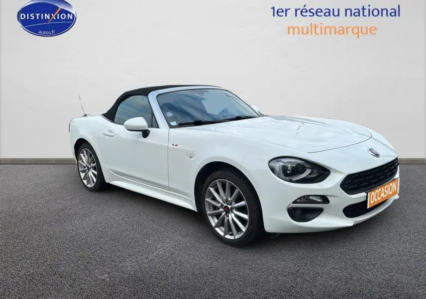 Fiat 124 Spider blanc vue 3/4 avant droit, capote noire fermée et jantes alliage 17 pouces visibles.